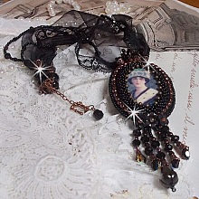 Pendentif Midnight Daisy avec un cabochon en bois repr&eacute;sentant une femme en chapeau Bleu, brod&eacute; avec des fleurs lucites, coupelles et facettes. Le tout est fini avec une dentelle Noire et un ruban